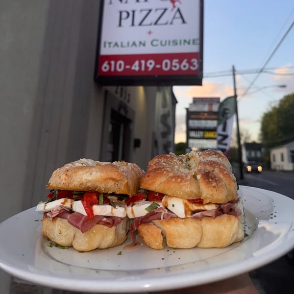 Two Italian sandwiches with prosciutto, mozzarella, roasted peppers, and basil on a white plate.