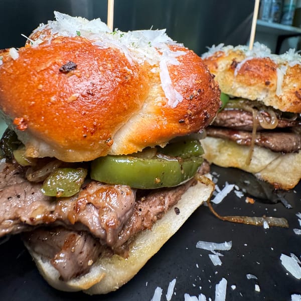 Two steak and pepper sliders on toasted buns, topped with shredded cheese and toothpicks.