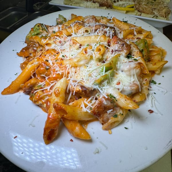 Penne pasta with chicken, broccoli, red sauce, and melted cheese on a white plate.