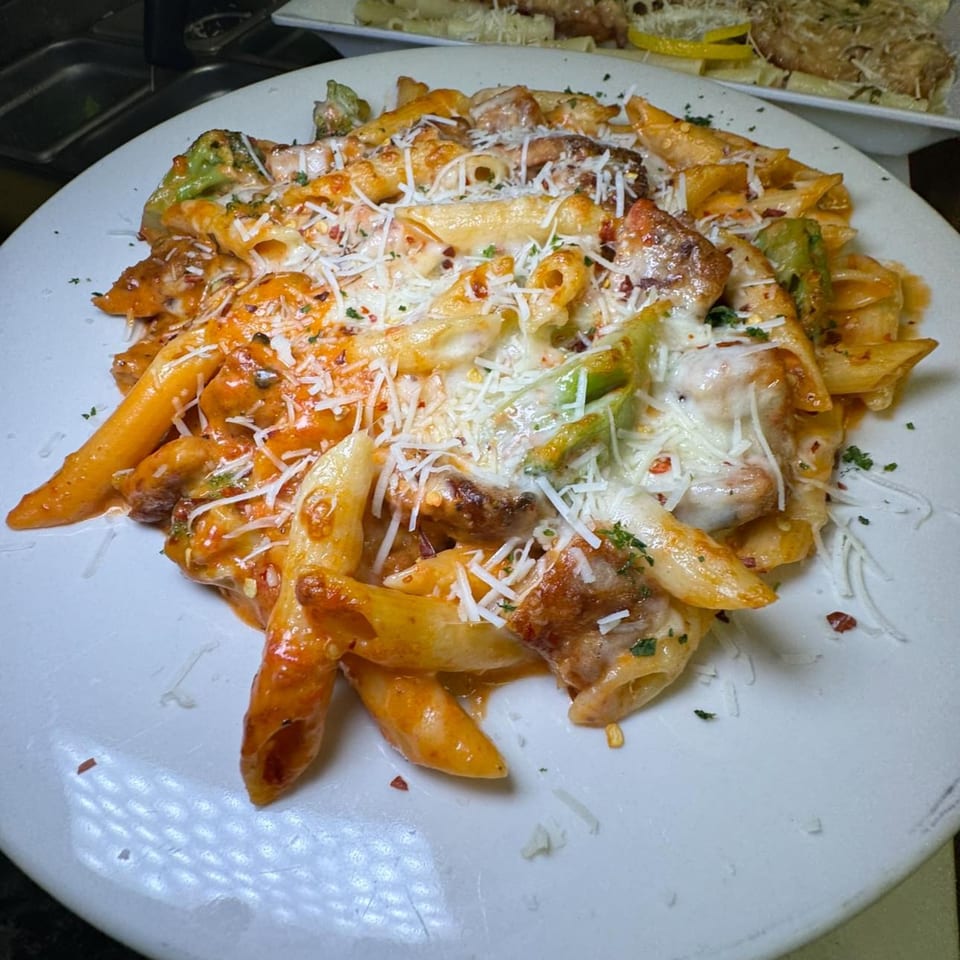 Penne pasta with chicken, broccoli, red sauce, and melted cheese on a white plate.