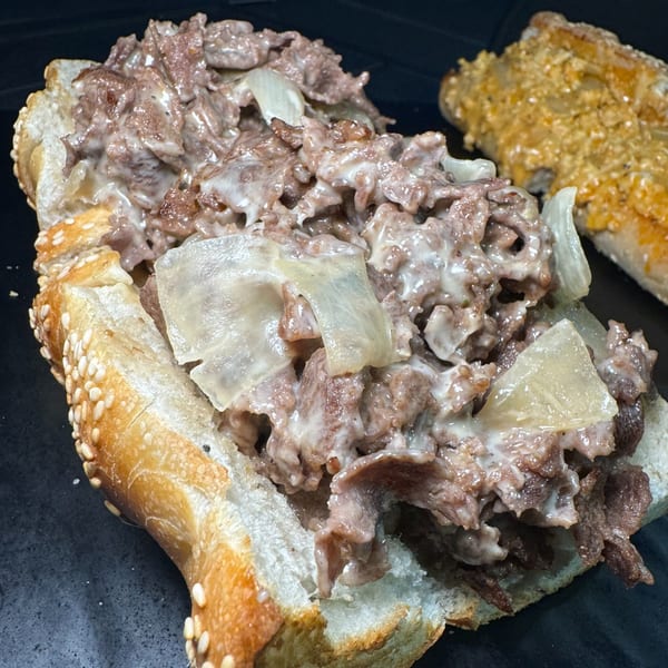 A close-up of a Philly cheesesteak sandwich with melted cheese and onions on a sesame seed bun.