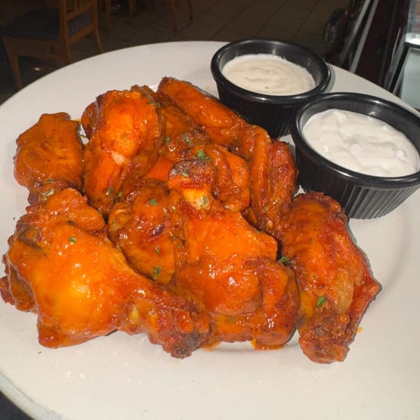 A plate of Napoli Pizza's buffalo wings, glistening with sauce, served with two ramekins of dipping sauce.
