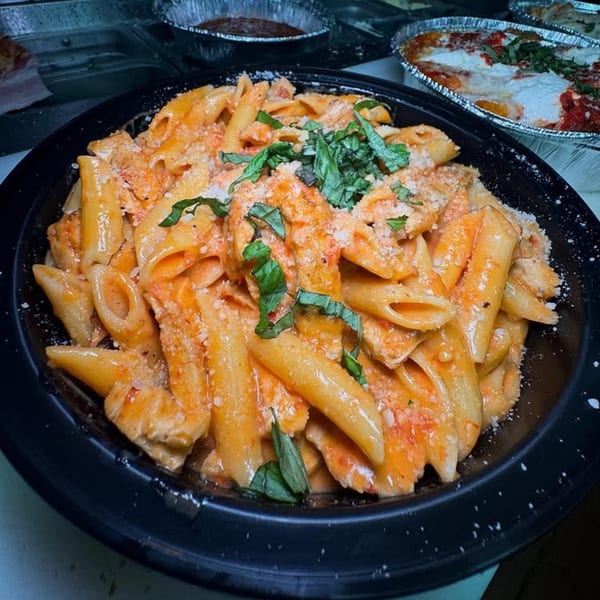 Penne pasta with creamy tomato sauce, chicken, parmesan, and fresh basil in a black bowl.