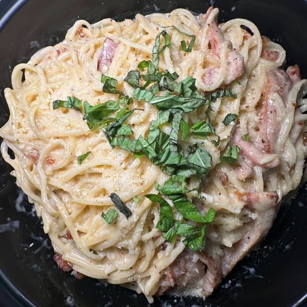 Creamy spaghetti carbonara with bacon, parmesan cheese, and fresh basil in a black bowl.